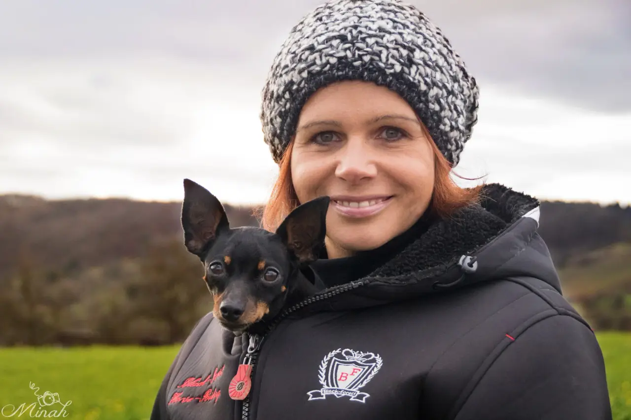 Tanja Schlipf mit Mütze, auf ihrer Schulter ein kleiner schwarzer Hund
