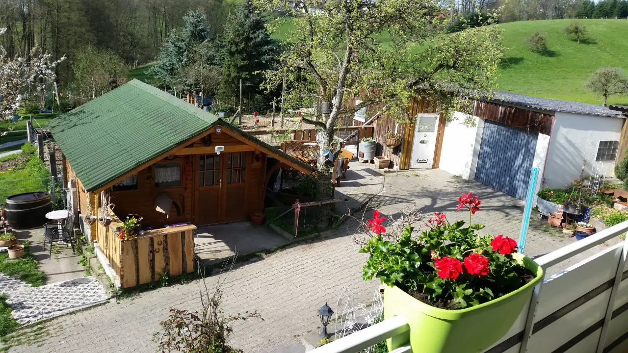 Blick von oben auf den Hof mit Holzhütte, Pflasterhof und grünen Wiesen dahinter