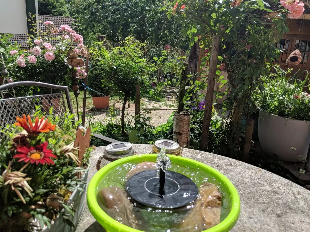 Kleiner Solarbrunnen zwischen Rosen und Blumen im Garten